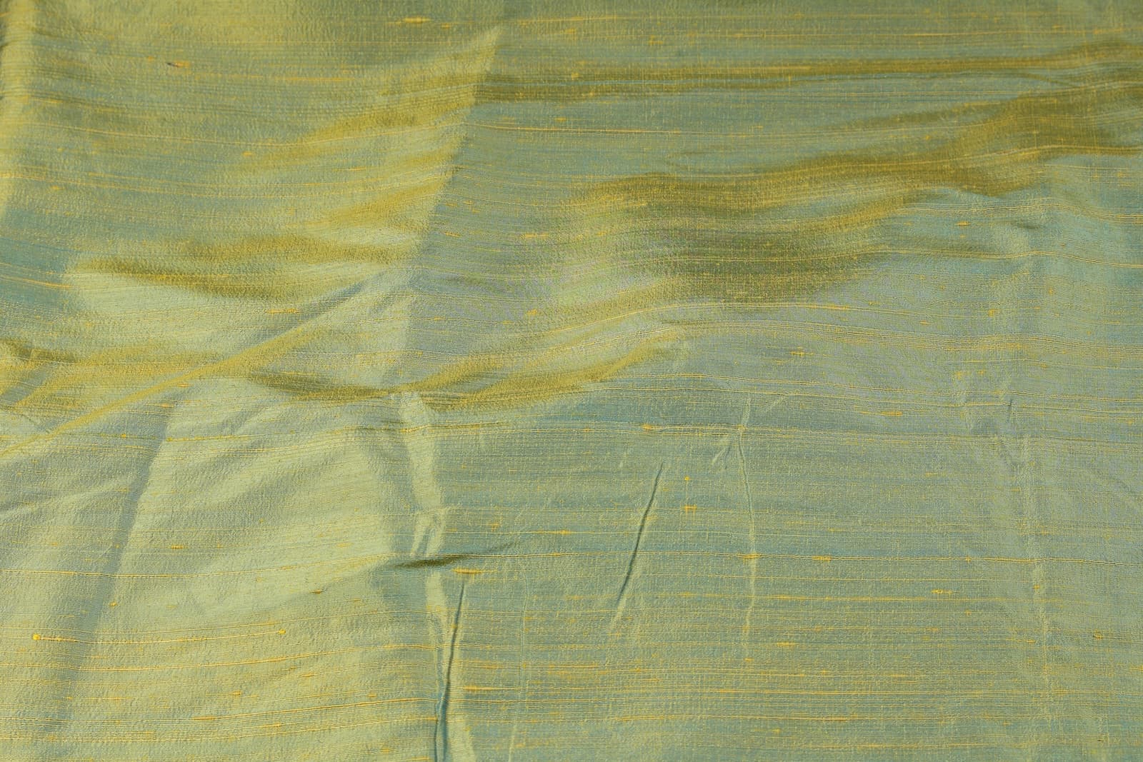 Close-up of Aqua Gold Dupion Silk Fabric showing natural slub texture, woven silk detail, and shimmering aqua-blue and gold tones
