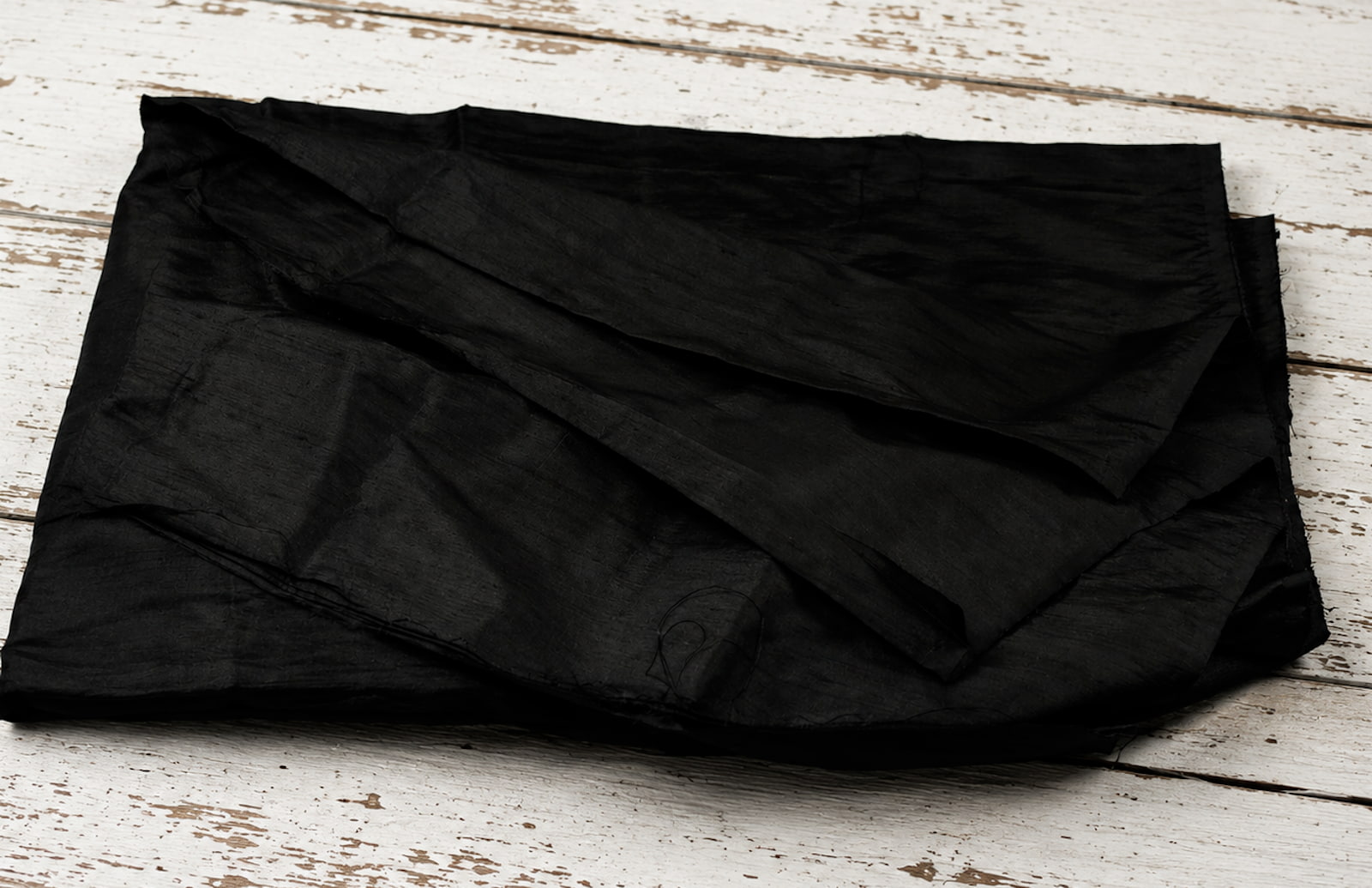 Black Dupion Silk Fabric displayed with flowing folds revealing natural slub texture and sophisticated black silk finish