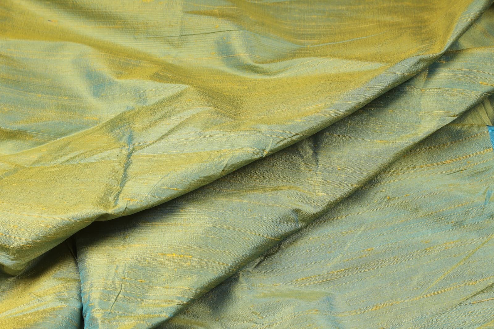 Aqua Gold Dupion Silk Fabric displayed with flowing folds revealing its iridescent aqua and gold colouring, silk texture, and luxurious finish