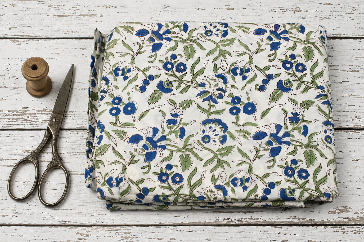 Hand block printed cotton fabric with blue floral blooms and green foliage on an ivory background