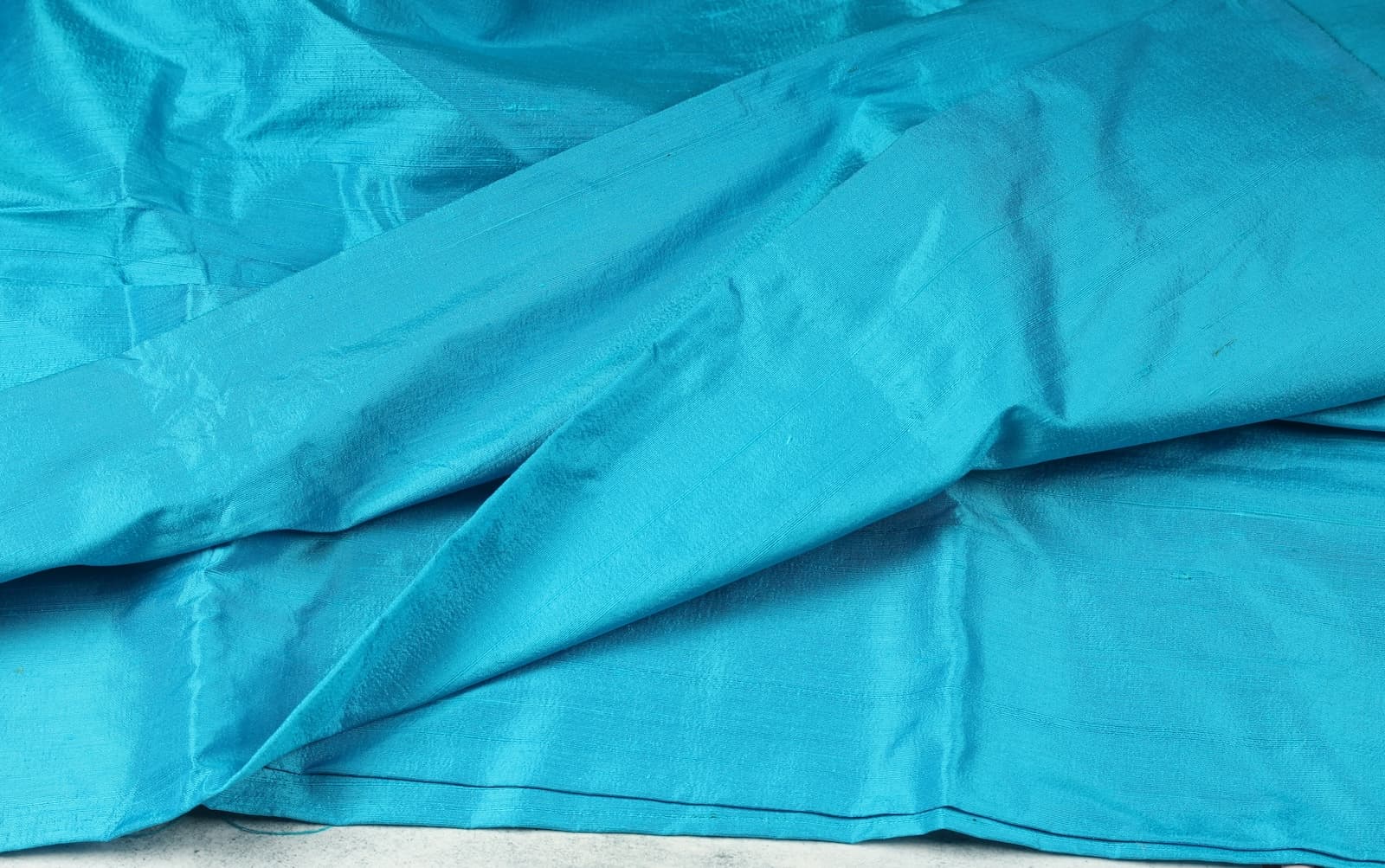Turquoise Dupion Silk Fabric displayed in flowing folds showing its vibrant colour and luxurious silk sheen