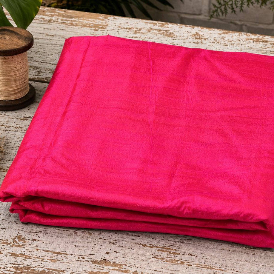 Electric Fuchsia dupion silk fabric folded on a tabletop showing vibrant pink raw silk with luminous sheen