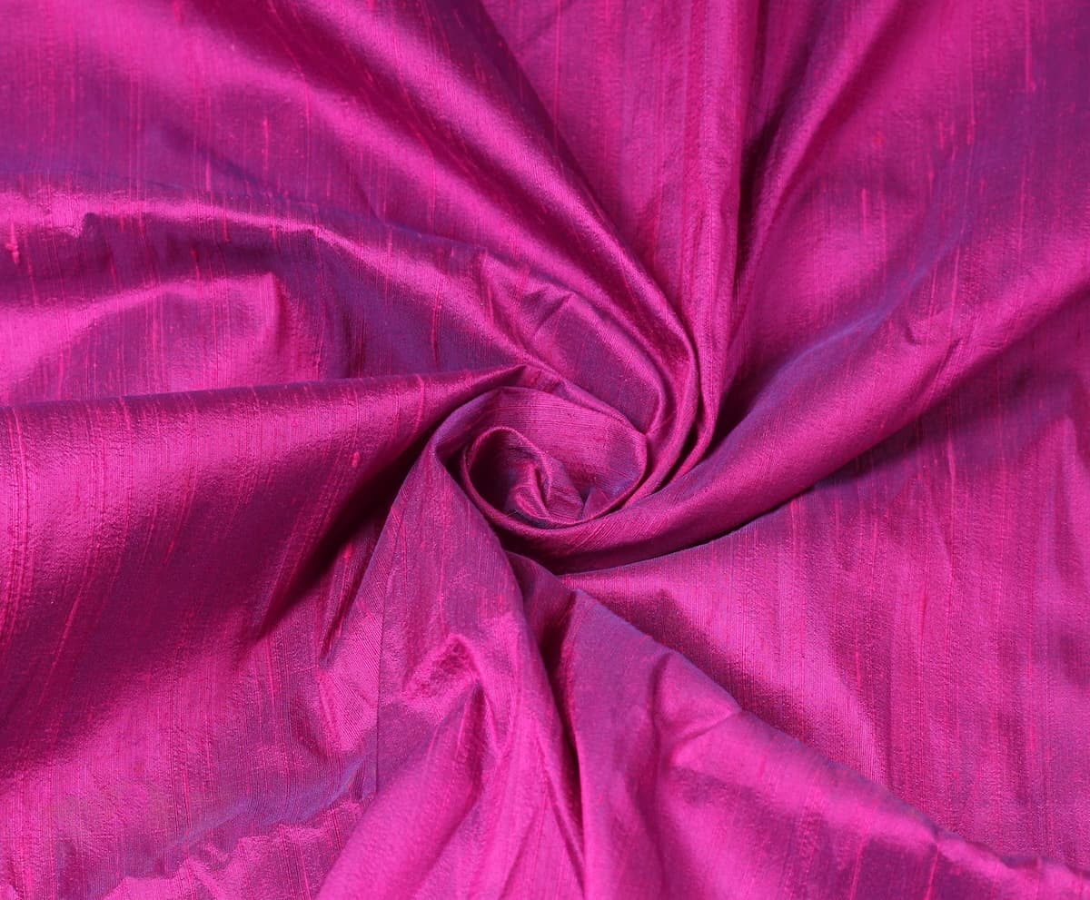 Fuchsia Magenta dupion silk fabric arranged in a swirl highlighting iridescent sheen, vibrant pink colour, and natural raw silk texture