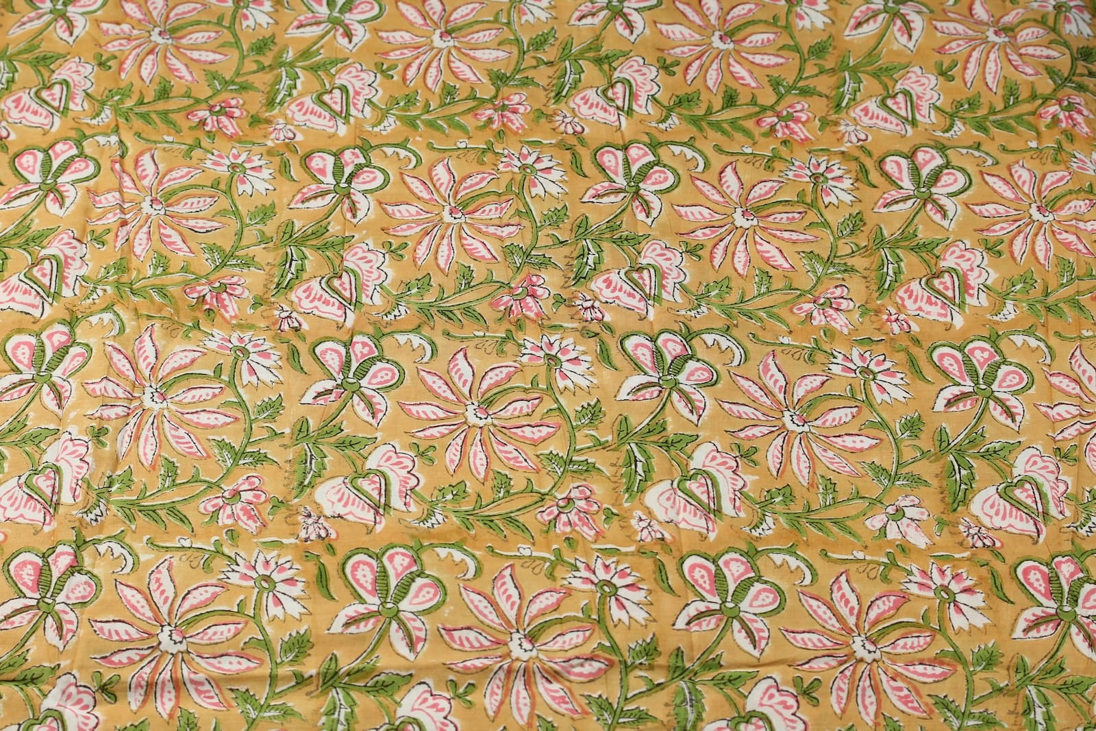 Golden floral block print cotton fabric featuring repeating pink flowers and trailing green botanical vines
