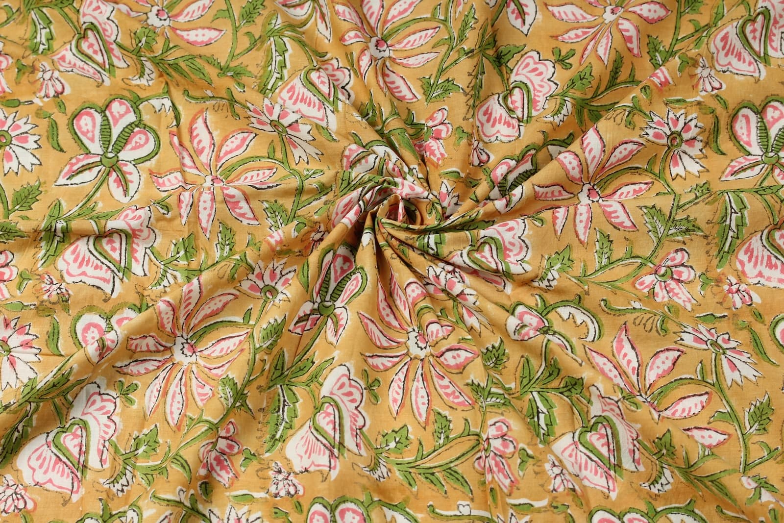 Hand block printed golden cotton fabric draped to showcase pink floral pattern and soft cotton texture