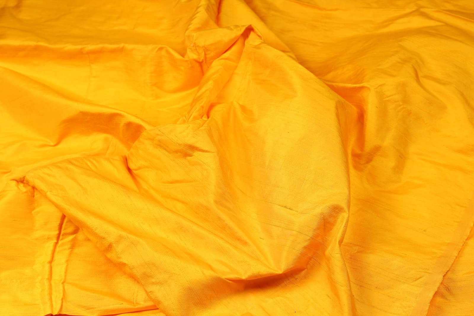 Golden Marigold Dupion Silk Fabric displayed in flowing folds showing its vibrant golden yellow colour and luxurious silk sheen