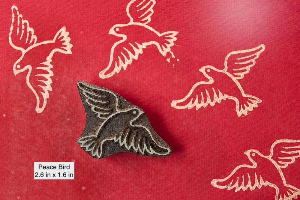 Hand carved peace bird wood printing block with flying bird motif stamped on red paper.