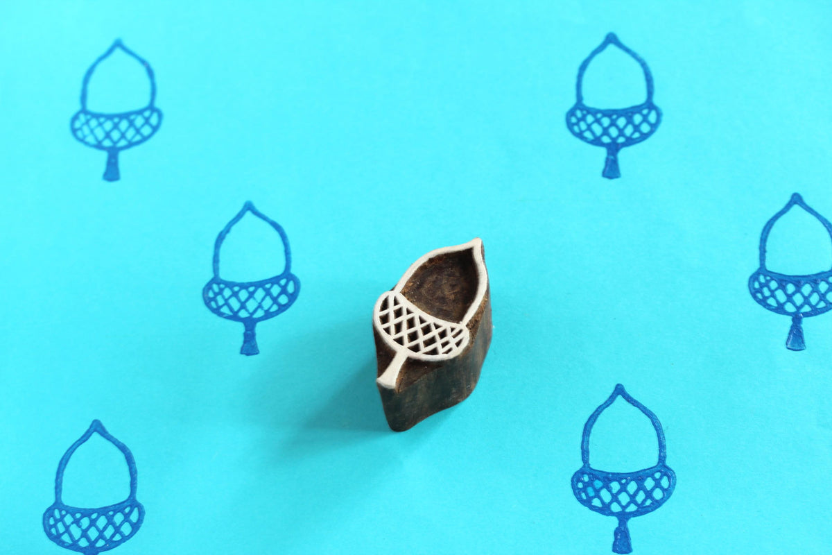 Hand carved wooden acorn printing block stamp shown with blue acorn prints on teal background.