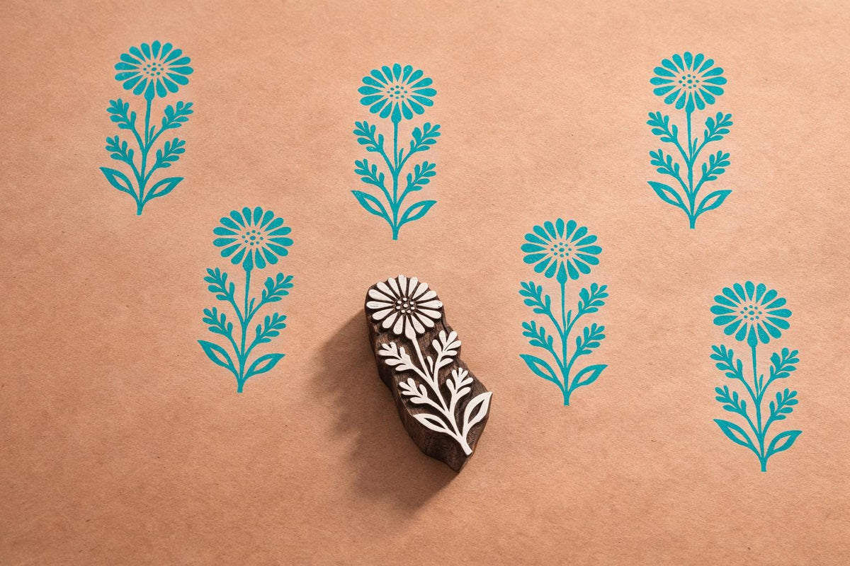 Hand carved wooden wildflower block printing stamp creating repeating floral pattern on kraft paper.