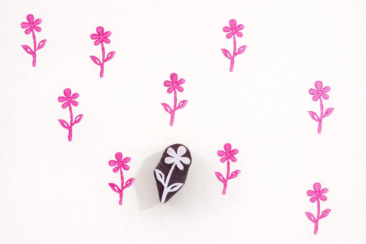 Small hand carved wooden flower block printing stamp creating repeating pink floral pattern on white background.