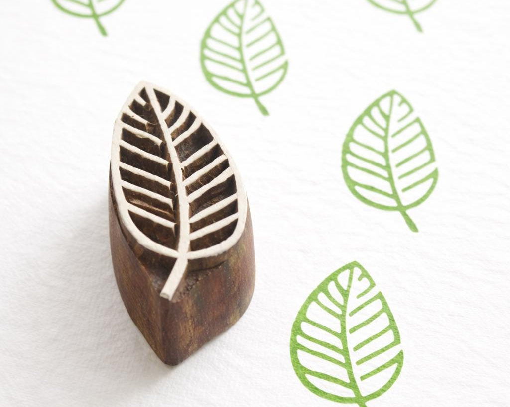 Hand carved Indian wooden printing block with a leaf design shown on white fabric with repeated green leaf prints.