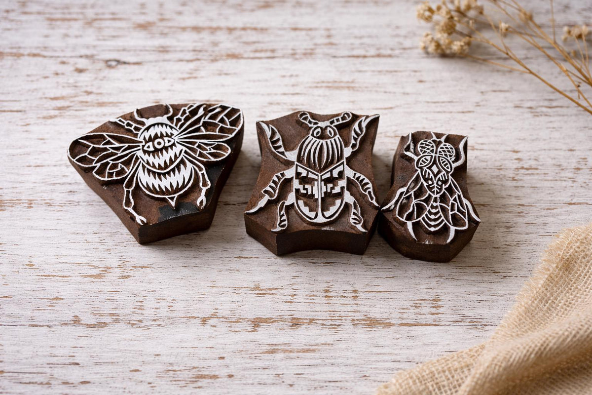 Set of three hand carved wooden insect block printing stamps featuring bee, beetle and fly designs on rustic white background.