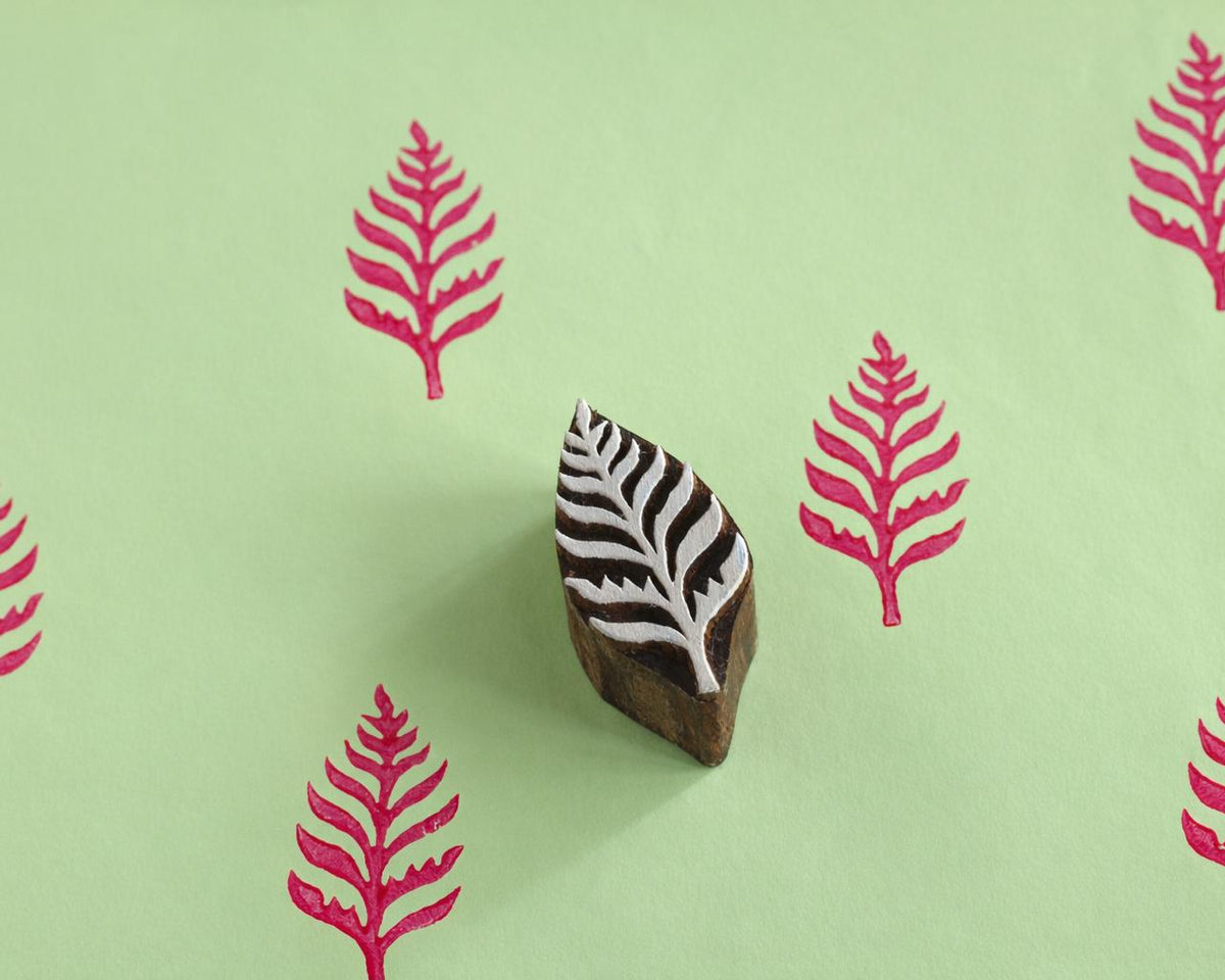 Hand carved wooden fern leaf printing block shown with pink fern prints on light green paper.