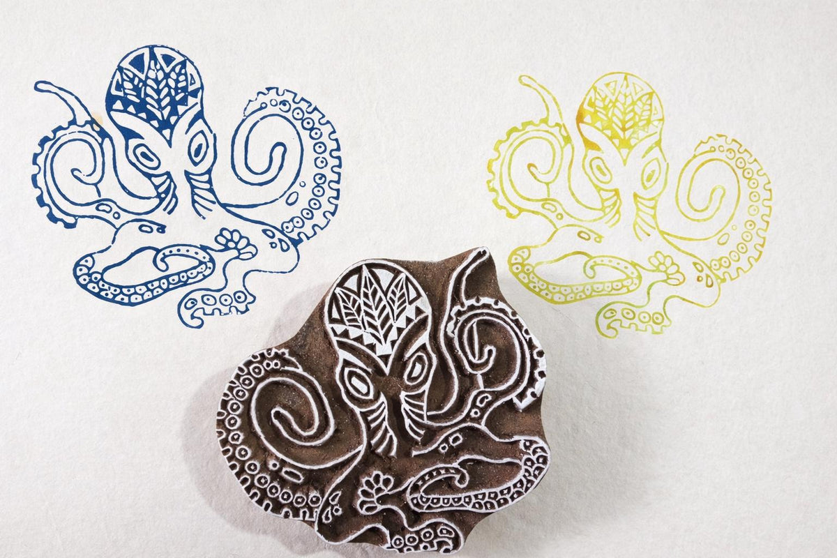 Hand carved wooden octopus block printing stamp with detailed tentacles shown with blue and yellow ink impressions.