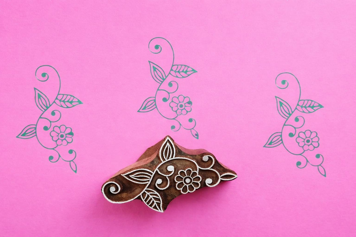 Hand carved wooden vine floral block printing stamp creating green vine prints on pink paper.
