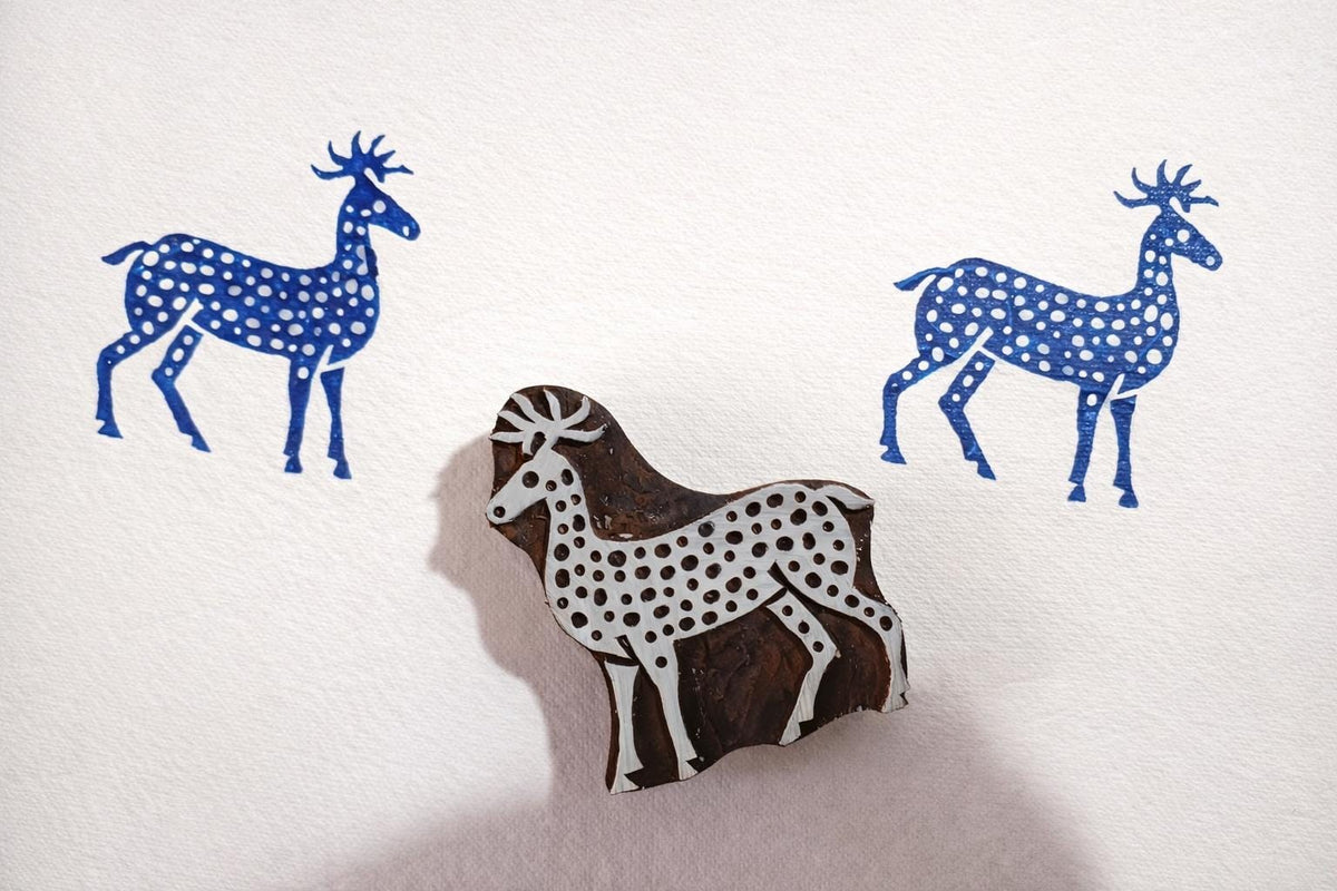 Hand carved wooden deer block stamp creating blue deer prints with dotted pattern on white paper.