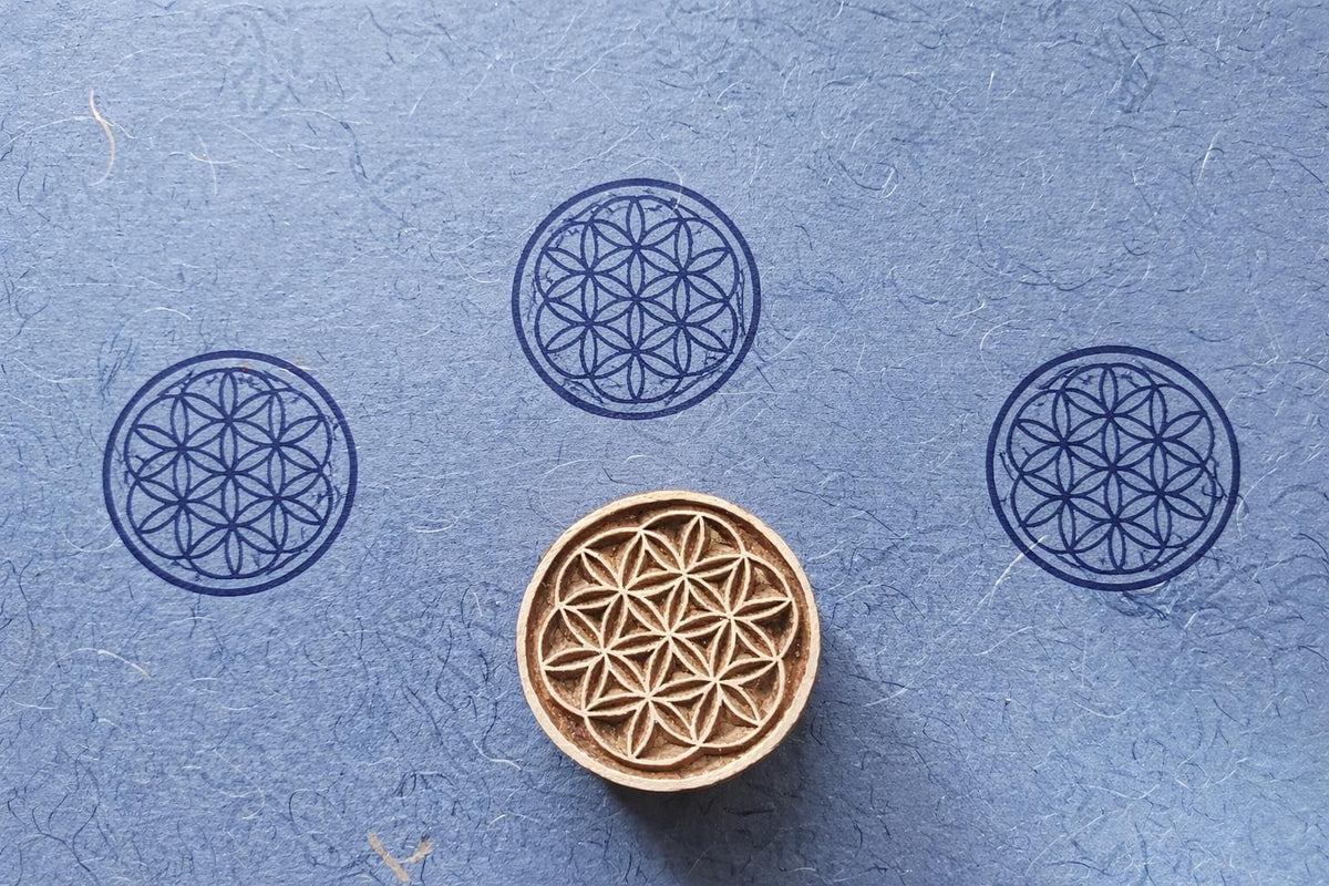 Hand carved wooden Flower of Life block printing stamp creating circular geometric prints on blue handmade paper.