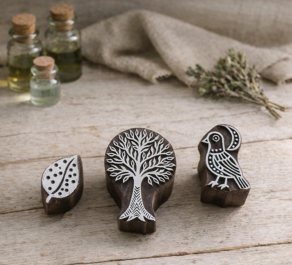 Hand carved wooden block printing stamps featuring tree, bird and leaf designs arranged on a rustic wooden table.