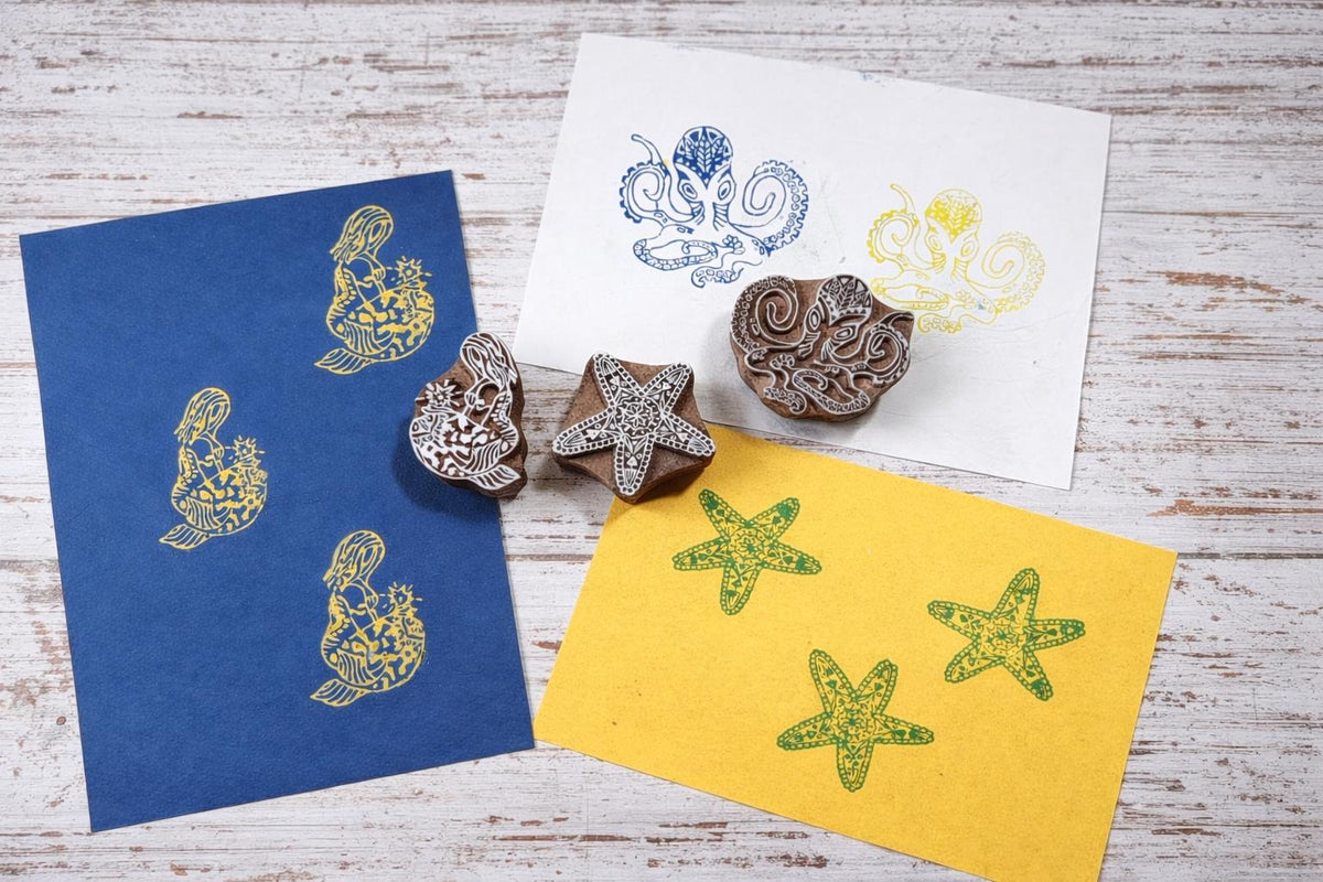 Wooden octopus, starfish, and mermaid block printing stamps displayed with colorful printed samples on paper.