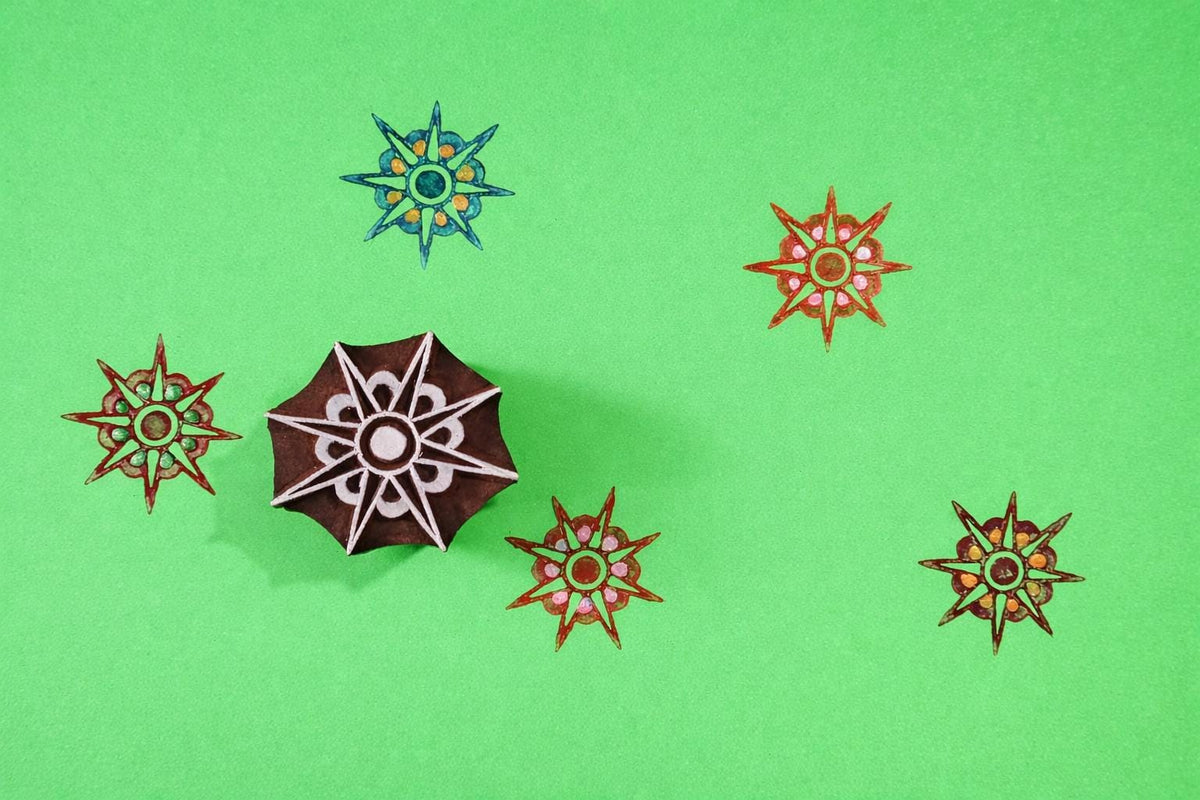 Hand carved wooden starburst mandala block printing stamp shown with multicolor star prints on green background.