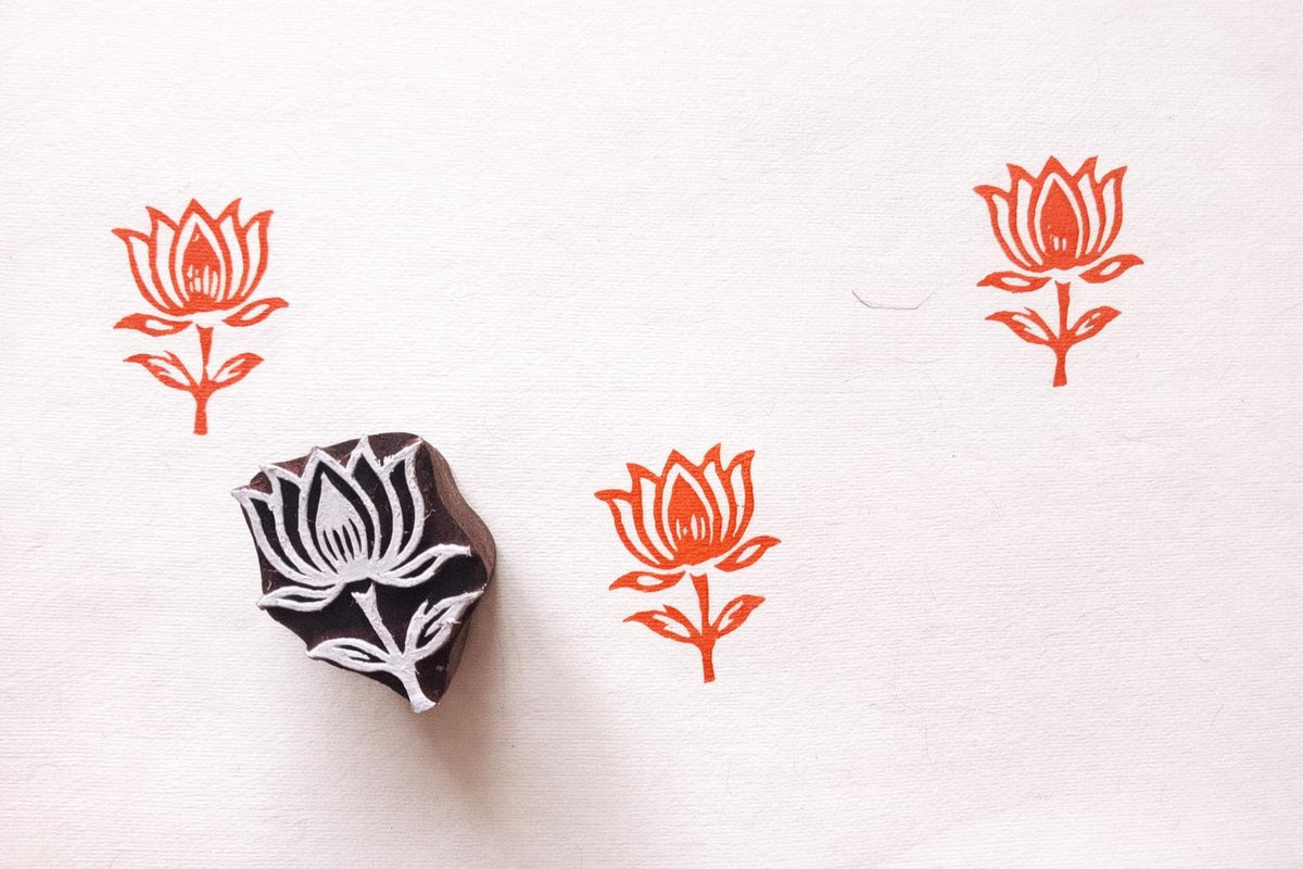 Hand carved lotus flower wooden block printing stamp creating orange lotus prints on textured white paper.