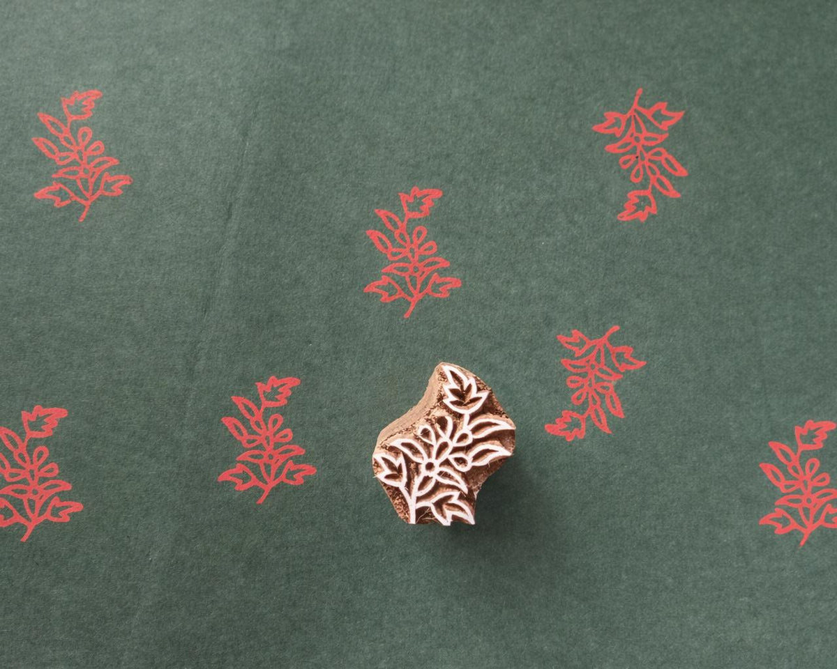 Hand carved wooden floral block printing stamp producing red plant motif prints on dark green paper.