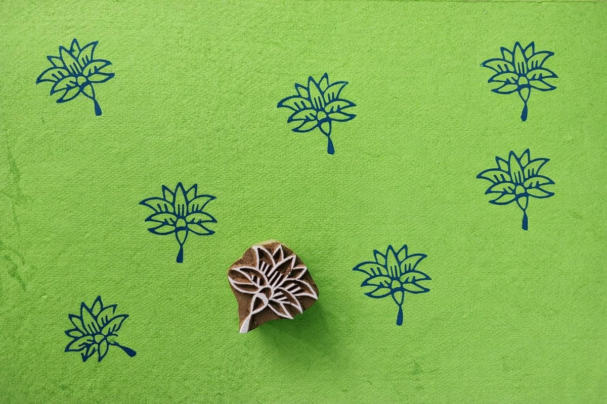 Wooden lotus flower block printing stamp creating dark blue lotus prints on bright green paper.
