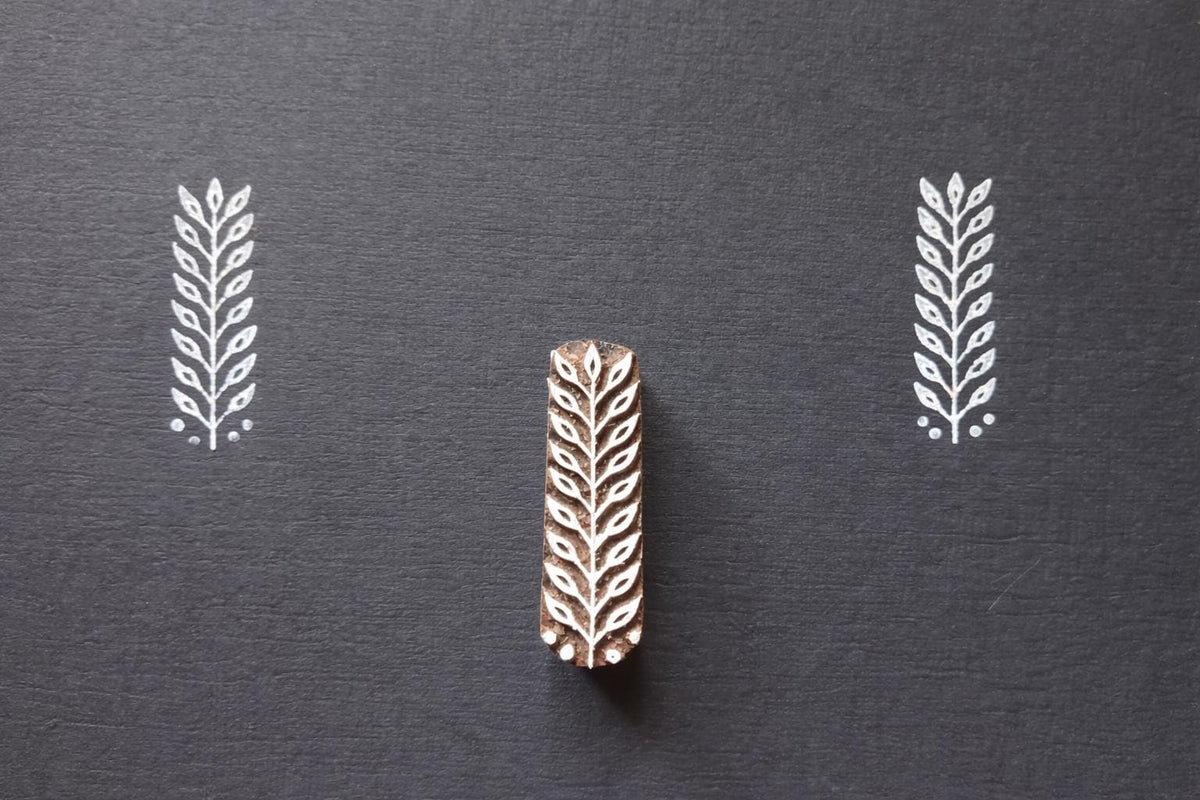 Hand carved leaf textile stamp made from wood showing white leaf prints on dark paper.