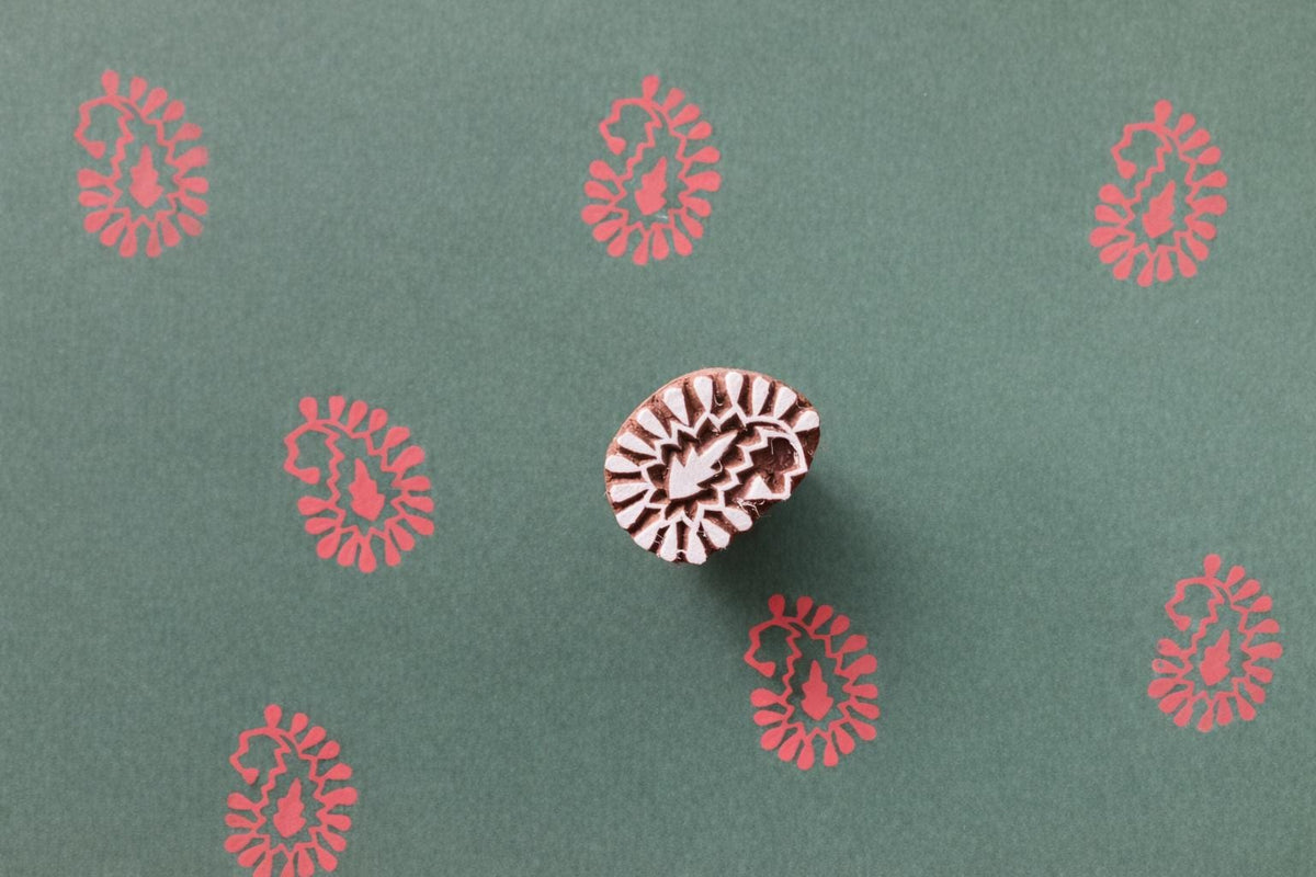 Paisley bloom wooden block printing stamp creating red prints on green handmade paper.
