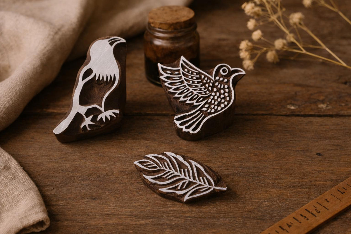 Hand carved wooden block printing stamp set featuring bird and leaf motifs displayed on rustic wooden table with natural linen cloth and dried flowers.