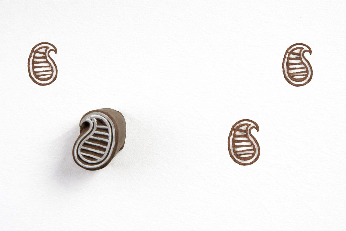 Hand carved wooden striped paisley block printing stamp creating brown paisley prints on white paper.