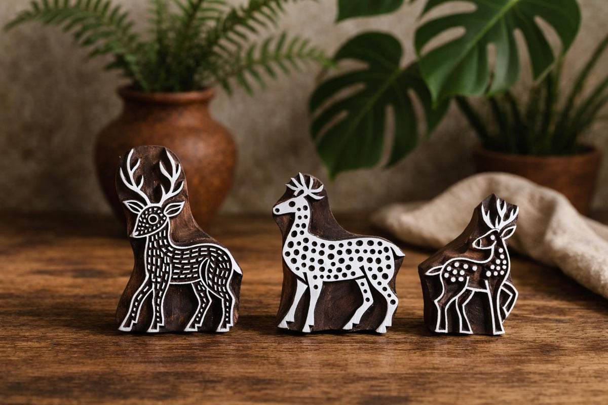 Set of three hand carved wooden deer block printing stamps on rustic wooden table with plants in background.