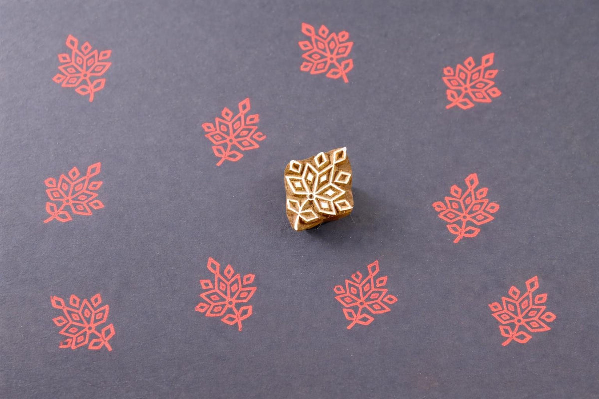 Wooden block printing stamp creating red leaf pattern prints on dark blue paper.