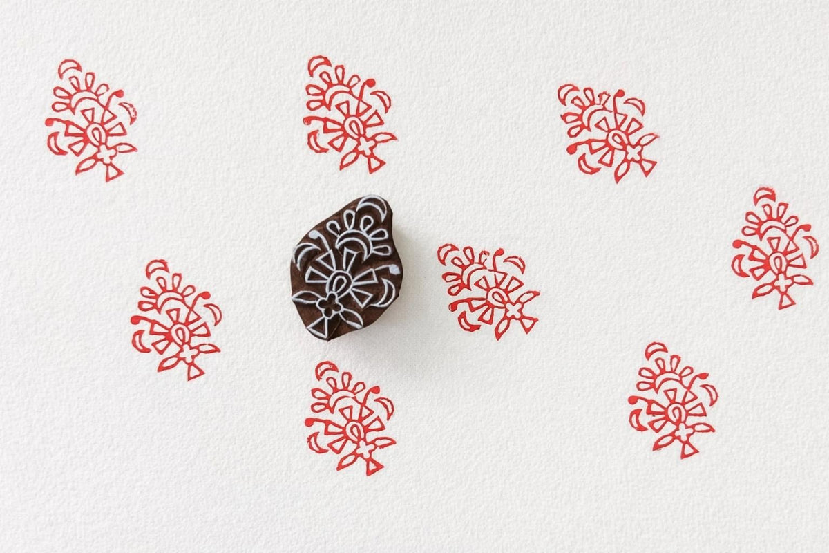 Hand carved wooden block stamp creating repeating red ornamental folk prints on white paper.