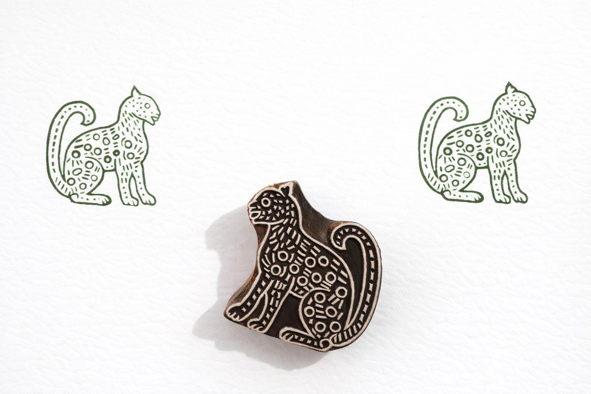 Hand carved wooden spotted leopard block printing stamp creating green wildlife prints on white paper.