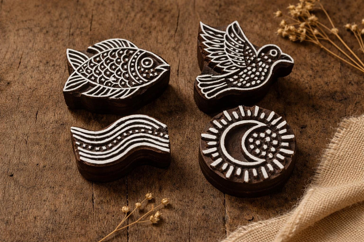 Hand carved wooden block printing stamps featuring bird, fish, moon and wave designs on rustic wooden table.