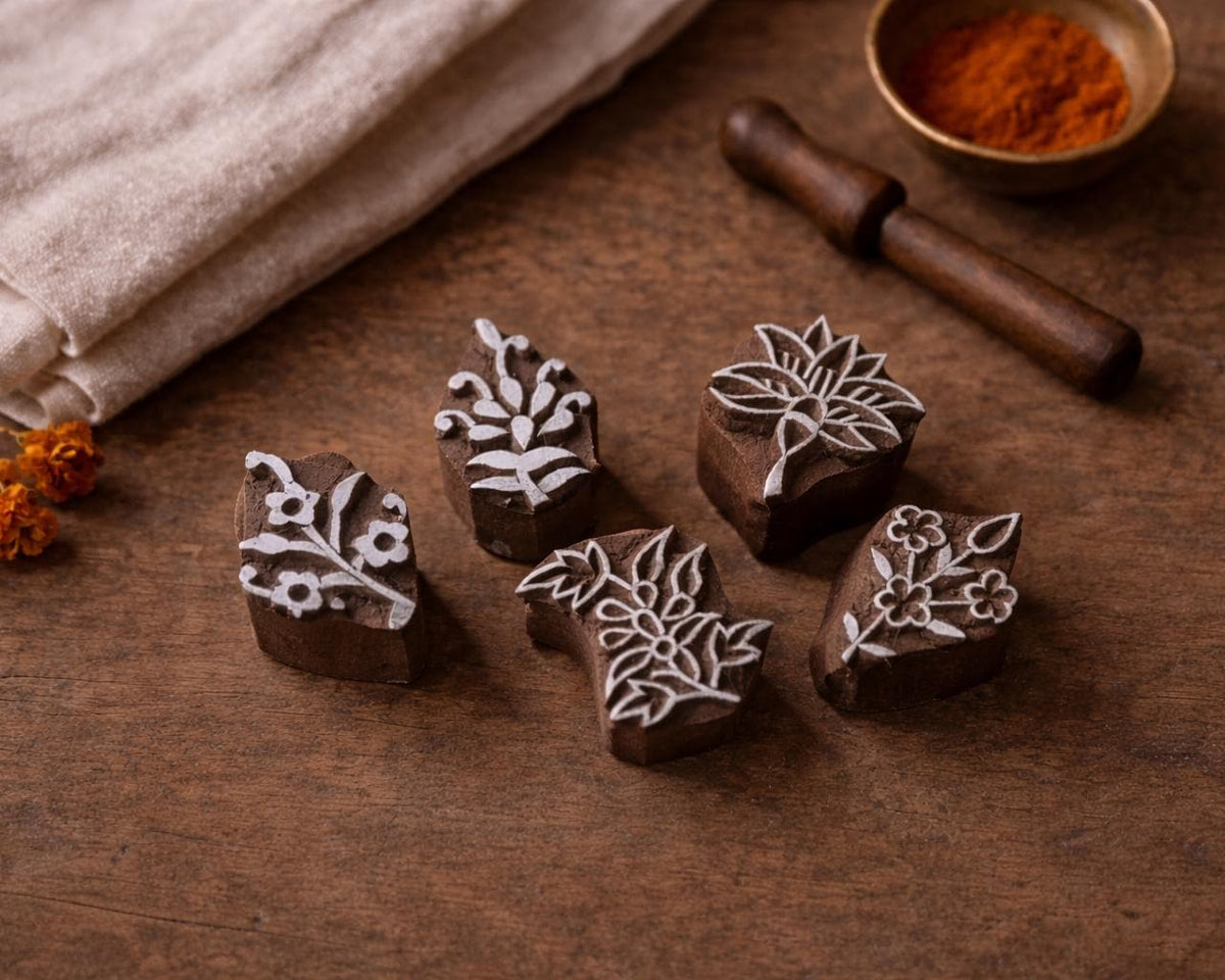 Hand carved Indian wooden block printing stamps with botanical flower designs arranged on a brown wooden table with linen cloth and spice bowl.