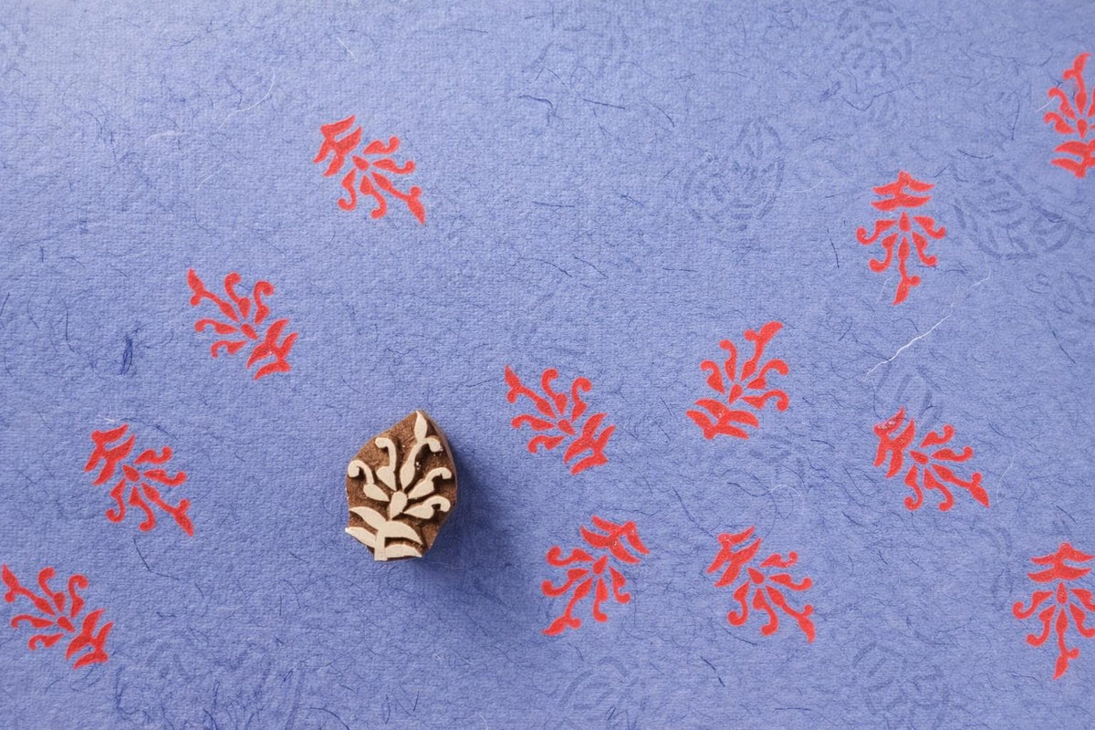 Hand carved wooden block printing stamp creating red botanical prints on textured blue paper.