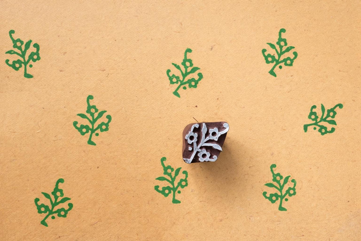 Wood block printing stamp making green botanical motif prints on textured yellow handmade paper.