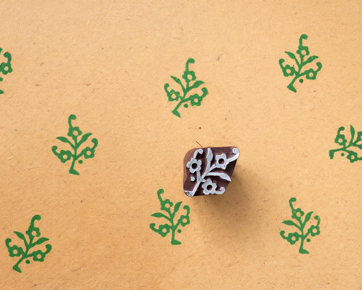 Wood block printing stamp making green botanical motif prints on textured yellow handmade paper.