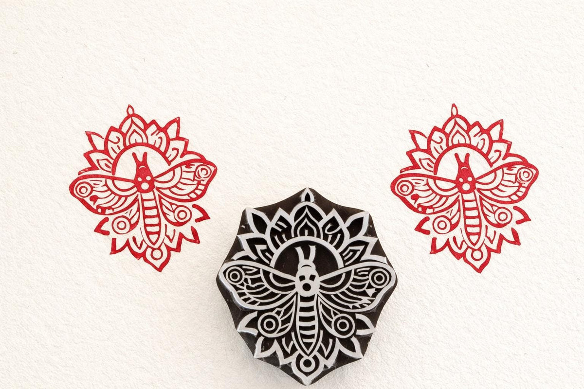 Hand-carved mandala moth stamp printing intricate symmetrical insect design on paper.