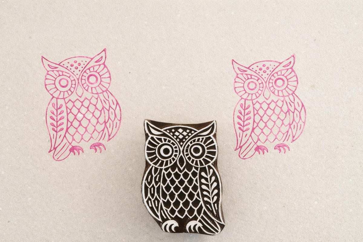 Hand carved wooden owl stamp with feather pattern design printed in pink ink on textured paper