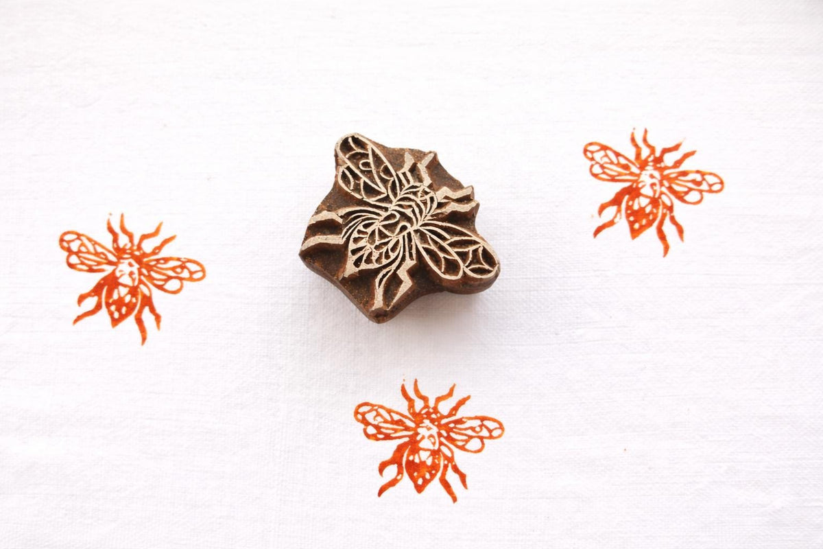 Hand carved honeybee wooden block printing stamp creating orange bee prints on white fabric background.