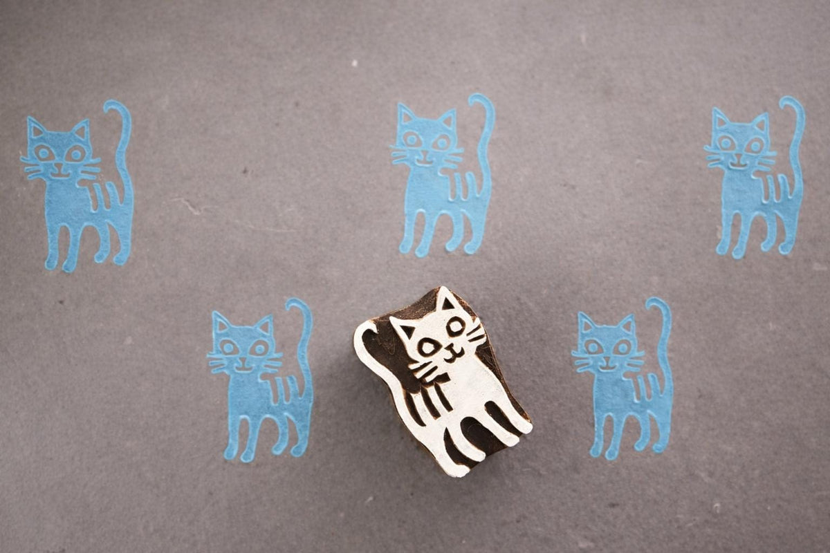 Bright tail cat wooden block printing stamp creating light blue cat prints on textured grey paper background.