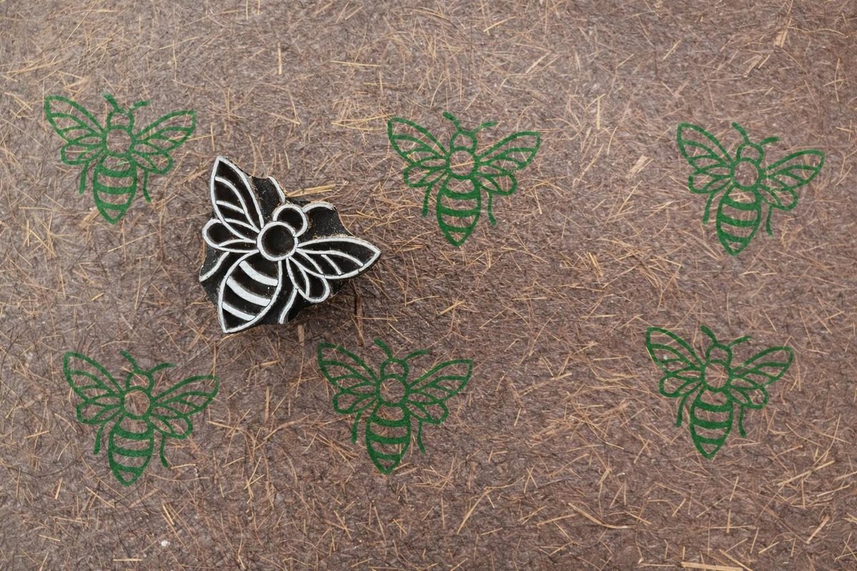 Bee wooden block printing stamp creating green bee prints on textured handmade paper.