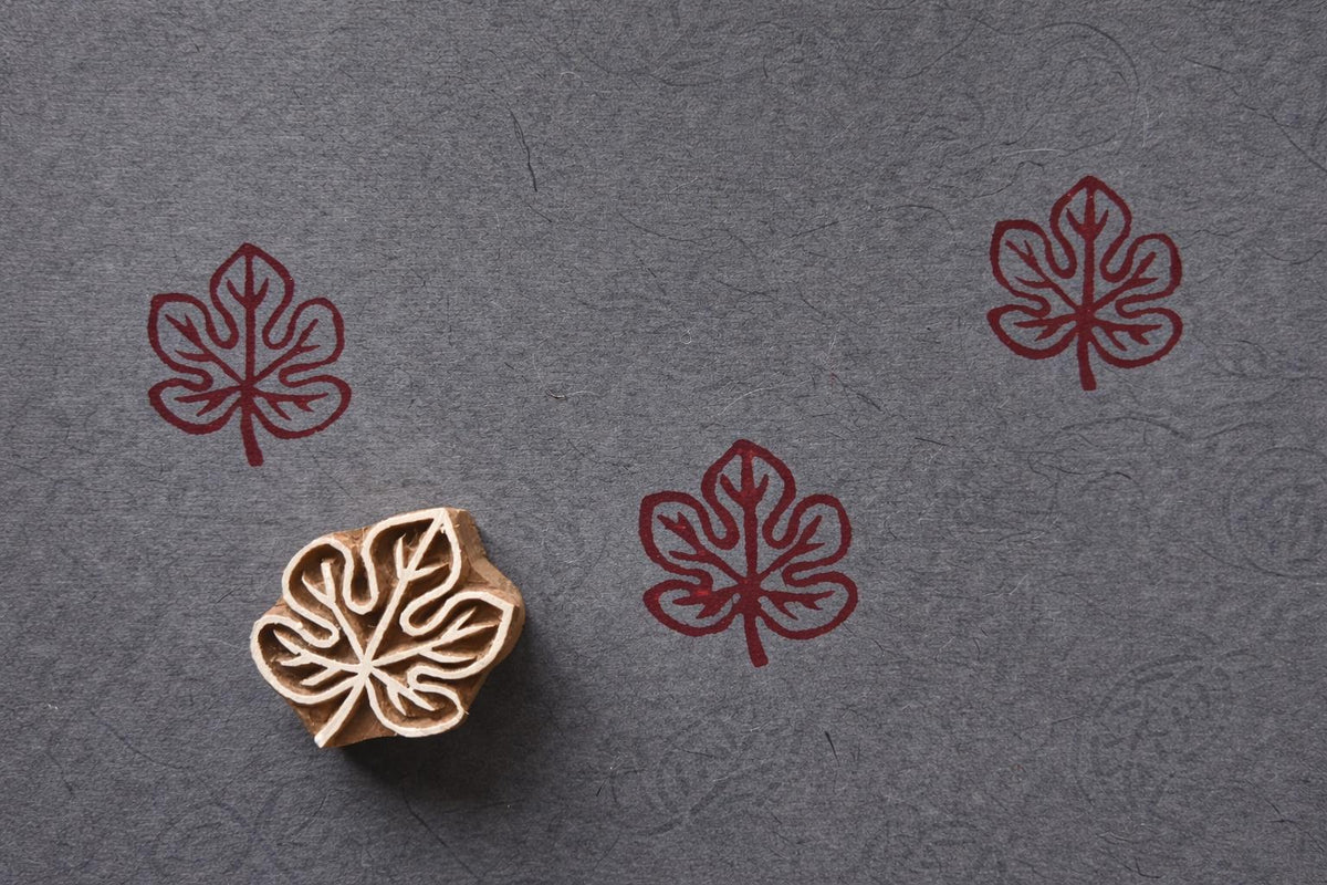 Hand-carved wooden maple leaf block stamp with red leaf prints on fabric in a minimalist nature style