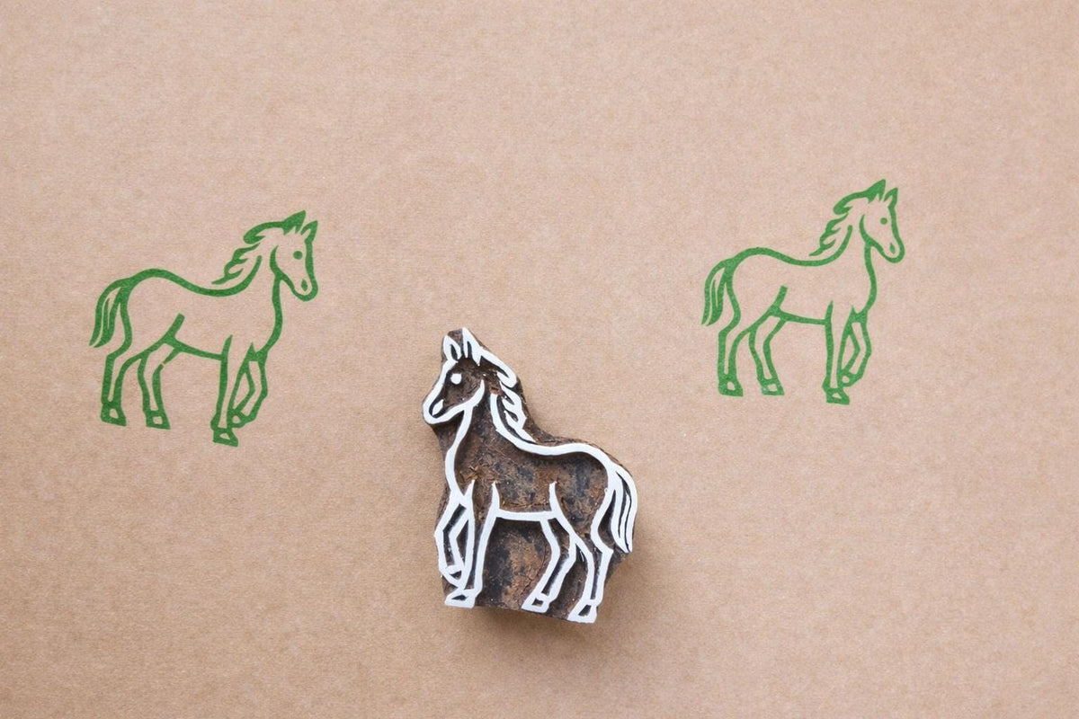 Hand-carved wooden horse block stamp with green horse prints on paper in a minimalist folk art style