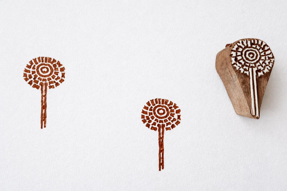 Hand carved wooden stamp with circular sunburst flower design and stem