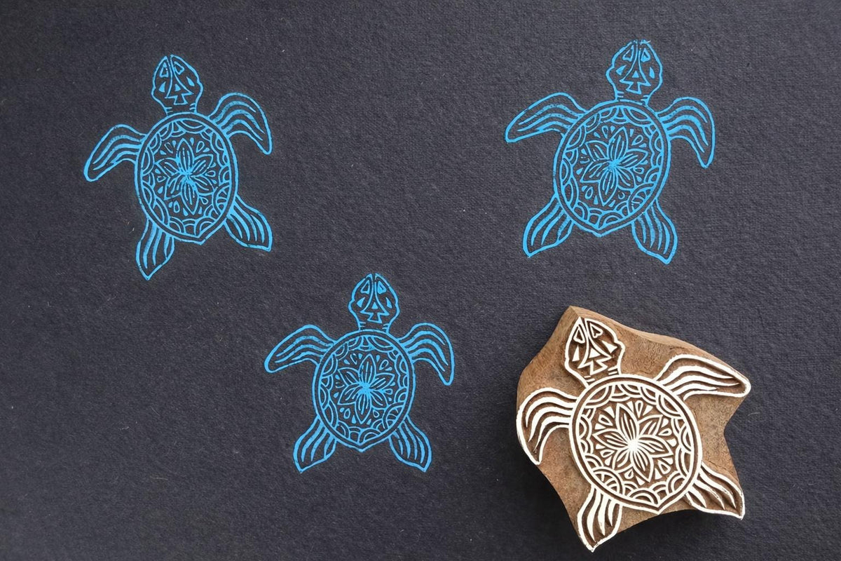Hand carved turtle block printing stamp creating decorative pattern on dark paper