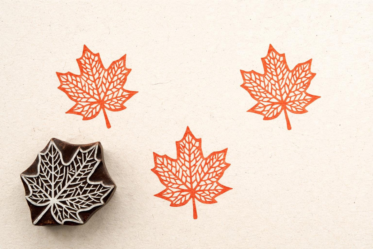 Maple Leaf wooden stamp producing intricate orange maple leaf prints on off white textured background